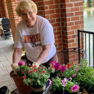 A woman smiles while tending to colorful flowers on a porch.