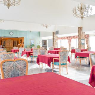 A spacious dining area featuring tables dressed in red tablecloths and elegant chairs, illuminated by a chandelier.