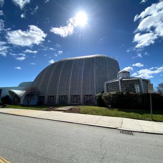 A modern architectural structure under a bright sun and cloudy sky.