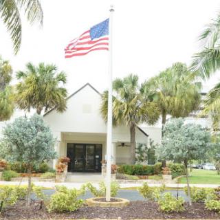 A view of a building featuring the American flag surrounded by palm trees and landscaped gardens.