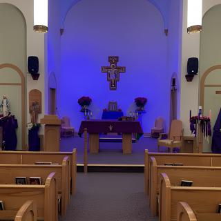 A church interior with wooden pews facing an altar, highlighted by blue lighting and a central cross.