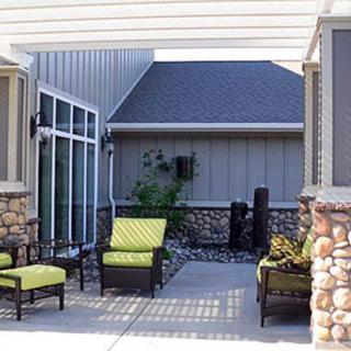 A modern patio with comfortable outdoor furniture under a pergola, featuring stone wall accents.