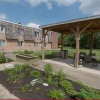 A landscaped garden area with a gazebo and outdoor seating near an apartment building.