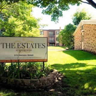 Entrance sign for 'The Estates' apartment complex with buildings and trees in the background.