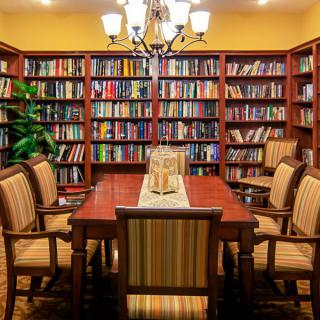 A cozy library room with a large dining table surrounded by bookshelves filled with books.