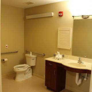 A clean and accessible bathroom featuring a toilet, sink, and large mirror.