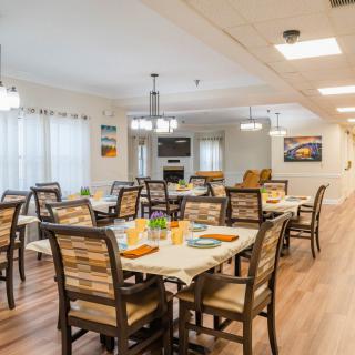 A bright and inviting dining room with neatly arranged tables and chairs, featuring warm decor and ample lighting.