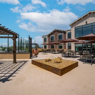 A spacious outdoor patio with ample seating and a sandpit, featuring a modern building under a clear blue sky.
