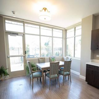 A bright dining area with large windows, a table, and chairs surrounded by natural light and indoor plants.