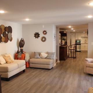A modern and cozy living room with sofas, decorative items on the wall, and wood flooring leading to an open kitchen area.