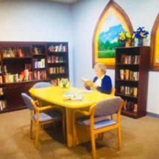 A person reading in a cozy library setting with bookshelves and a table.