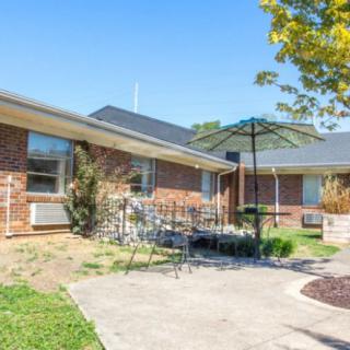 A brick residential building with a patio and outdoor furniture under an umbrella on a sunny day.