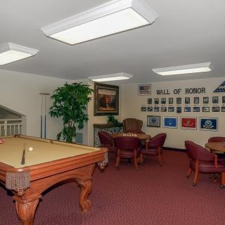 A cozy game room featuring a billiards table and seating area, adorned with a wall of honors and decorative lighting.