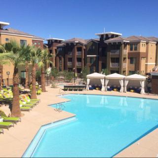A luxurious apartment complex featuring a large swimming pool surrounded by palm trees and poolside cabanas.