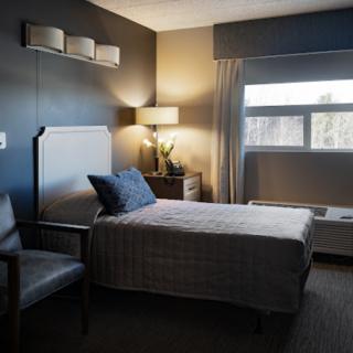 A modern hotel room with a comfortable bed, chair, and lamp by the window.