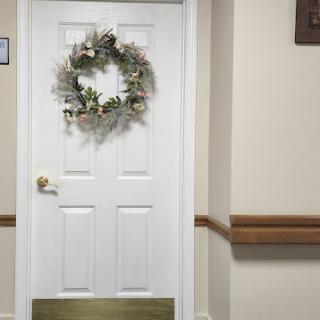 A decorated white door with a floral wreath, set in a beige hallway.