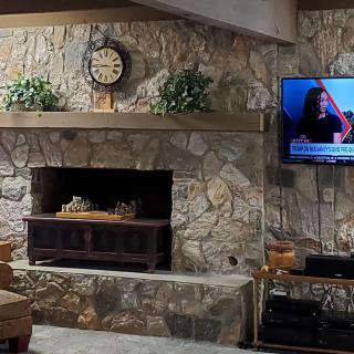 A cozy living room with a stone fireplace and a television mounted on the wall.