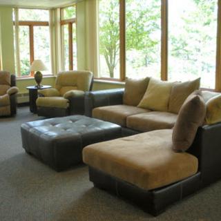 A cozy living room featuring a comfortable sofa, armchairs, and an ottoman, bathed in natural light from large windows.