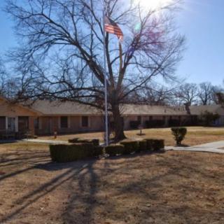 A sunny day with a flagpole in front of a building and tree.