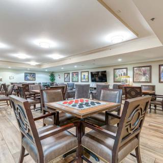 A spacious dining or activity area featuring several tables and chairs, with a checkers board on one table and framed artwork on the walls.