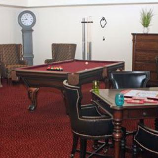 A cozy game room featuring a billiard table, chairs, and a standing clock on a carpeted floor.