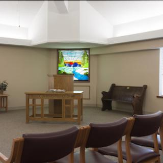 A peaceful chapel interior featuring wooden furniture and a vibrant presentation screen.
