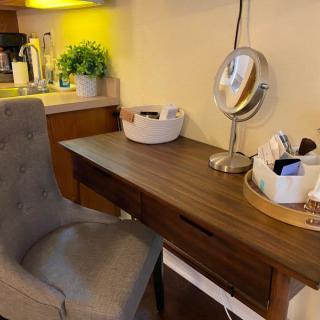 A cozy makeup station with a wooden desk, plush chair, and various accessories.