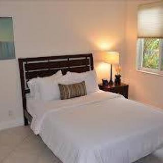 A minimalist bedroom with a neatly made bed, side table, and a lamp by the window.