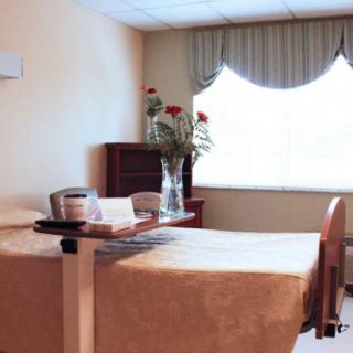 A hospital room featuring a bed, a vase with flowers, and natural light from the window.