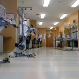 An empty hospital hallway with medical equipment and fluorescent lighting.