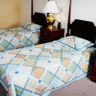 A cozy bedroom with two twin beds featuring colorful quilted bedding, accompanied by a wooden nightstand and a lamp.