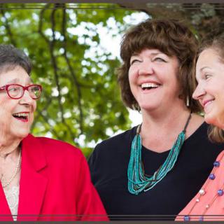 Three women sharing a joyful moment outdoors under the trees.