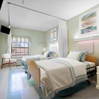 A clean and modern hospital patient room featuring two beds, light green walls, and natural light.