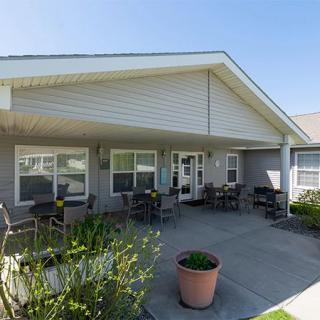 A cozy entrance with outdoor seating and plants, framed by a gabled roof.