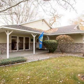 A suburban house with a covered porch and a flag, surrounded by autumn foliage.