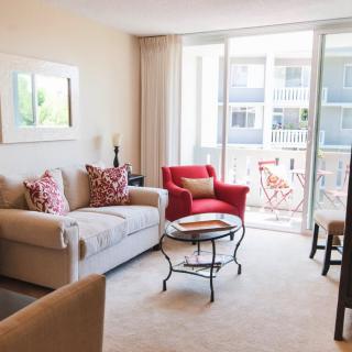 A bright and inviting living room with a comfortable sofa, red armchair, and coffee table overlooking a balcony.