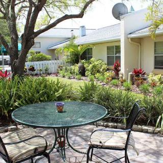 A serene backyard patio with a glass table and chairs surrounded by lush landscaping.