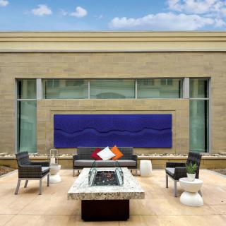 A modern outdoor patio with stylish furniture and a fire pit, framed by a large piece of wall art.