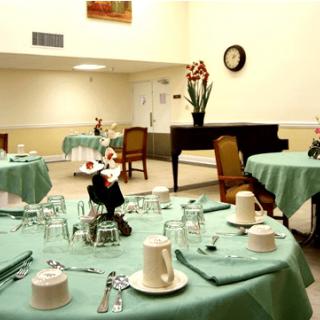 A well-set dining room with tables covered in green tablecloths, featuring cups and glasses, and a piano in the background.