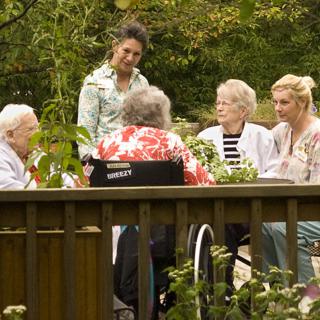 A group of seniors and a caregiver conversing in a garden setting.
