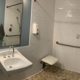 An accessible bathroom with a sink, mirror, grab bars, and a folding seat.