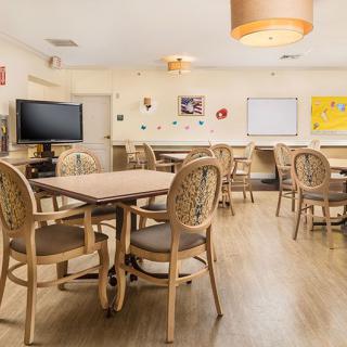 A cozy dining area with neatly arranged tables and chairs, featuring a wall-mounted television and decorative elements.