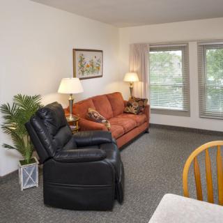 A cozy living room featuring a couch, recliner, and two lamps near large windows.