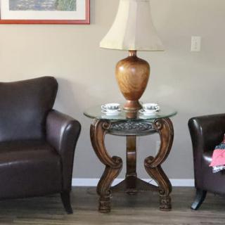 A cozy living room setup featuring a glass-top table with an elegant lamp, flanked by two comfortable leather chairs.