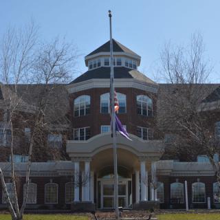 A large brick building with a central entrance and a flagpole in the front.