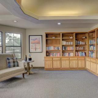 A cozy library room with wooden bookshelves, a comfortable seating area, and large windows.