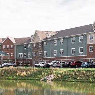 A residential building with a parking lot and a lake in the foreground.