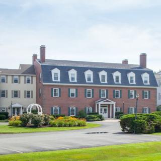 A large brick building with multiple windows surrounded by greenery under a clear sky.