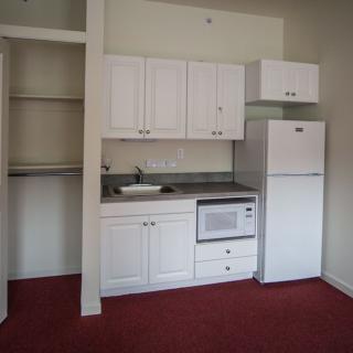 Compact kitchenette with white cabinets and appliances in an apartment.