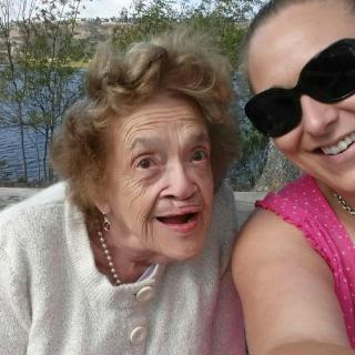 A selfie of an elderly woman and a younger woman smiling outdoors.